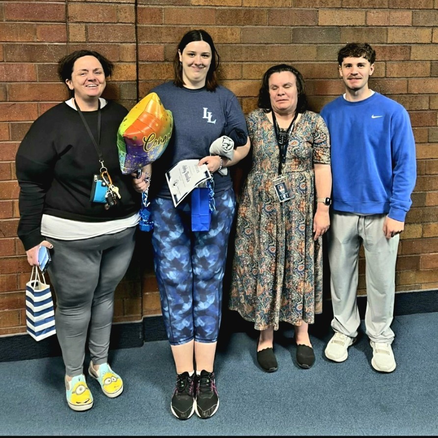 Abby, her mom, Mrs. Smith, and Coach Cannon posing for a picture in the hallway