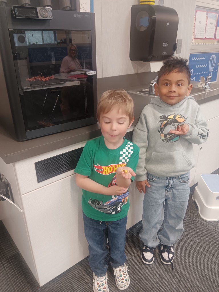 2 boys in front of a 2d printer holding 3d printed animals