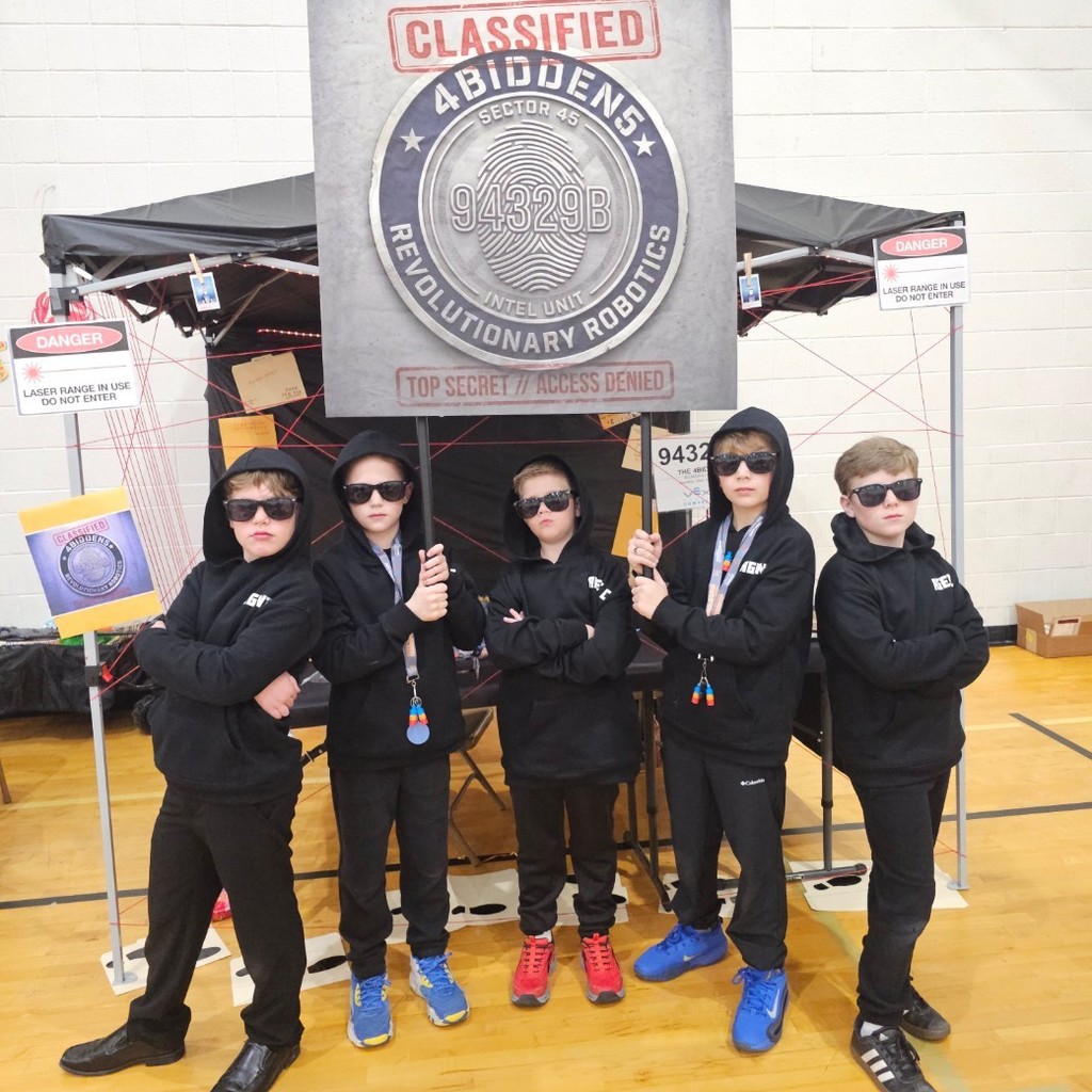 Five students in black hoodies and sunglasses pose at a spy-themed VEX IQ team display with a “4BIDDEN5” sign.