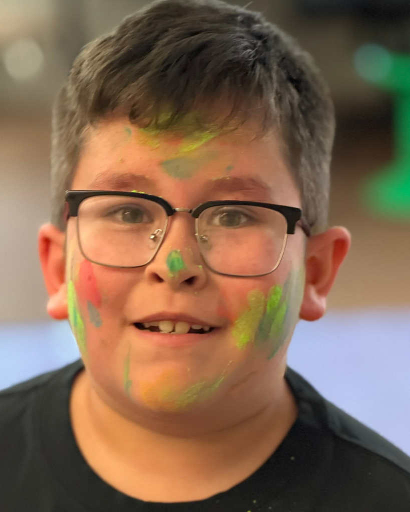 A  student with a colorful face smiles at the camera. 