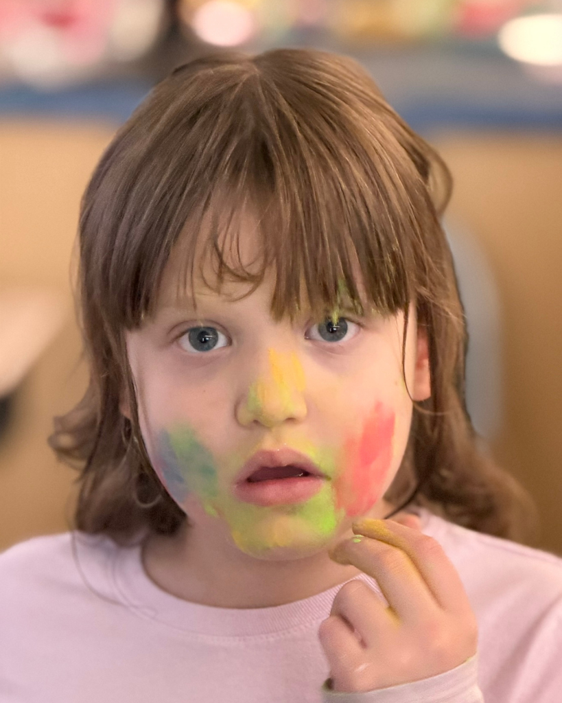 A  student with a colorful face smiles at the camera. 