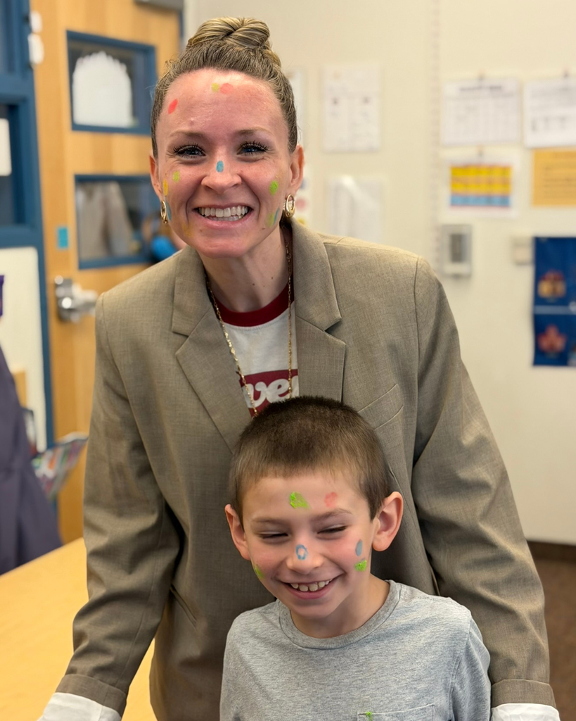 A teacher and student with colorful faces smile at the camera. 
