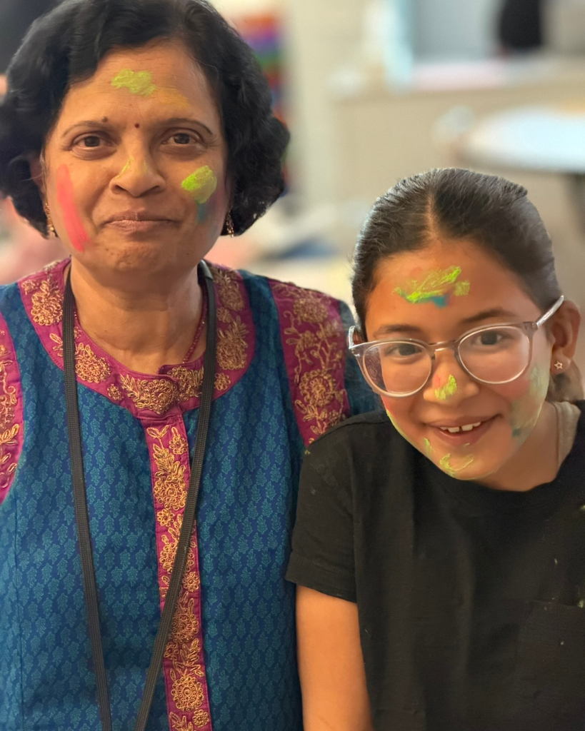 A teacher and student with colorful faces smile at the camera. 