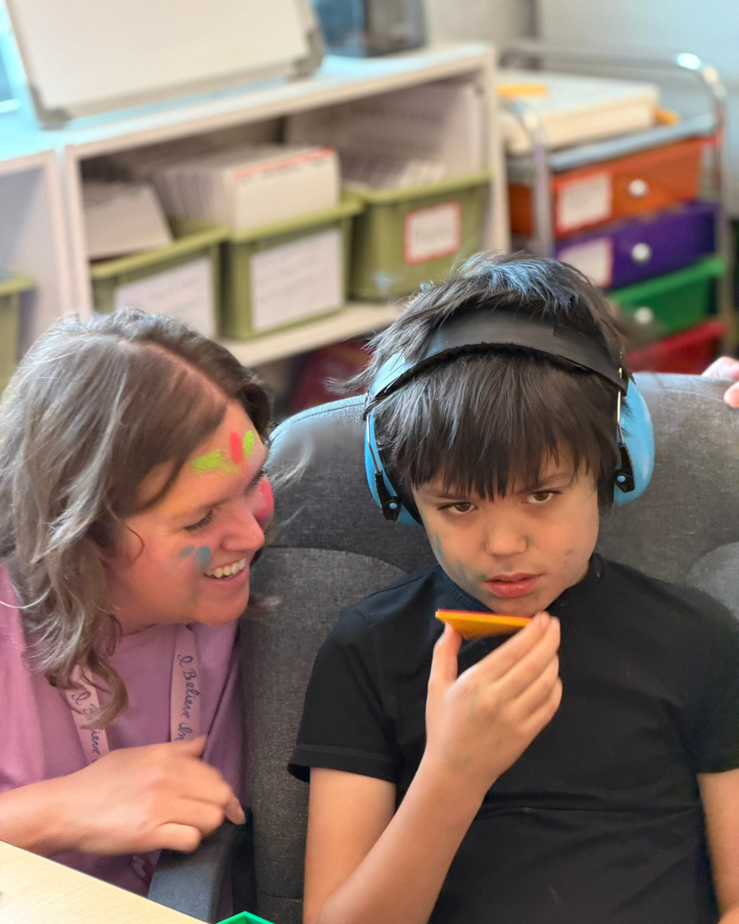 A teacher and student with colorful faces smile at the camera. 