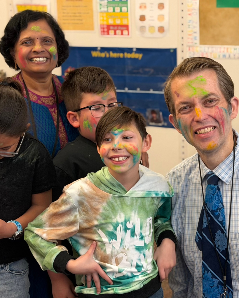 A teacher and student with colorful faces smile at the camera. 