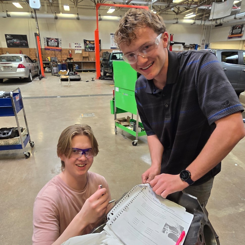 students smiling for a picture by the engine they are working on