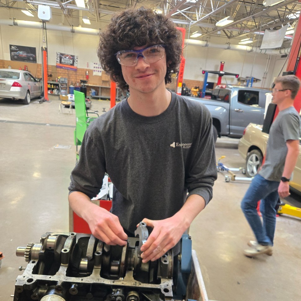 A student smiles as he works on an engine