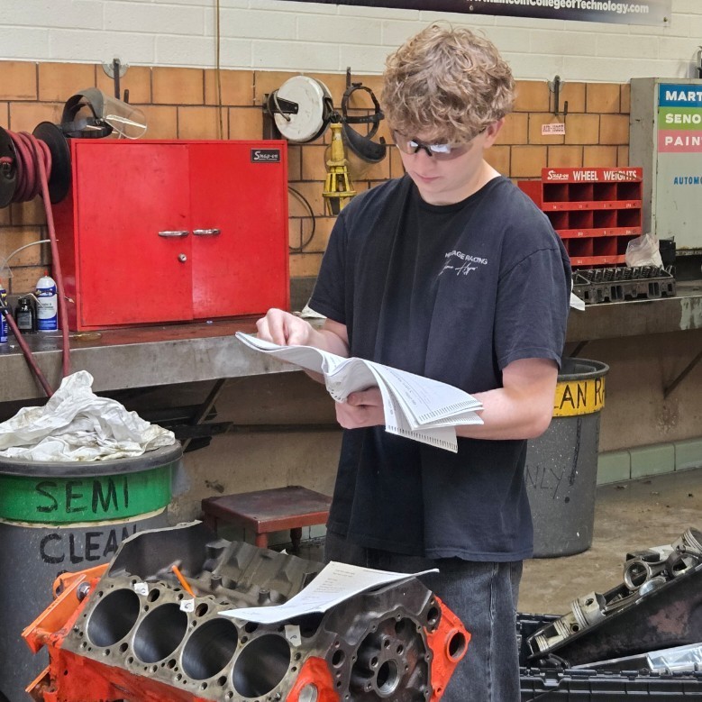 a student looking at instructions as he works on an engine