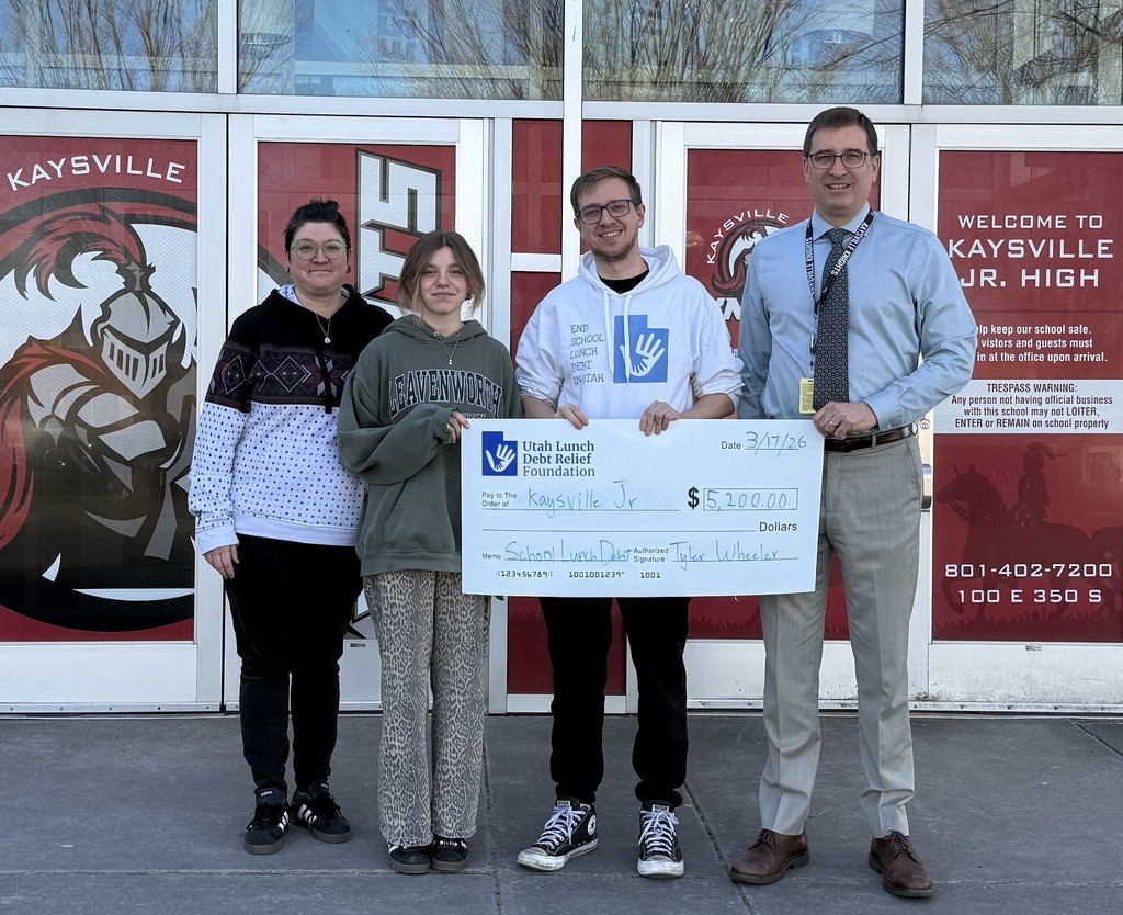 image of 4 people standing in front of kaysville junior high holding a check from utah lunch debt relief