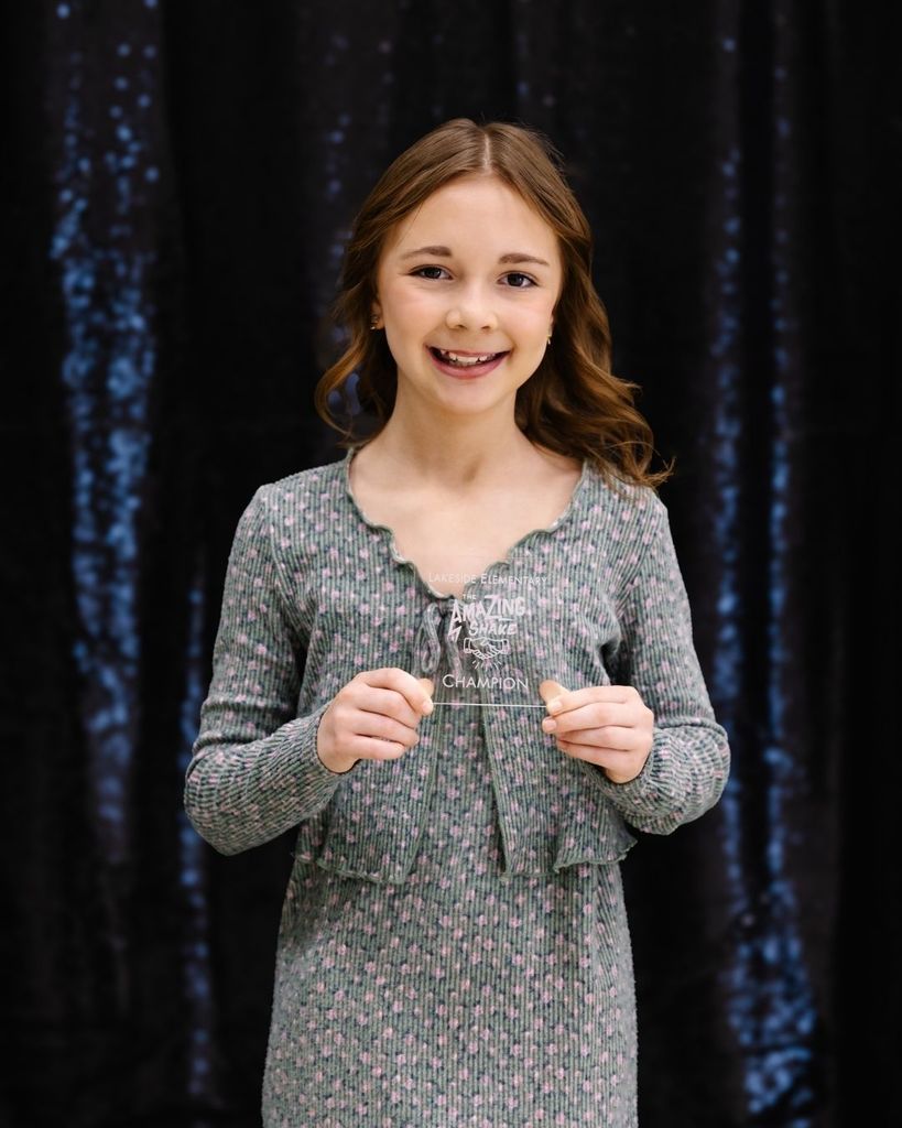 A student holds up a clear glass trophy that says "The Amazing Shake Champion."