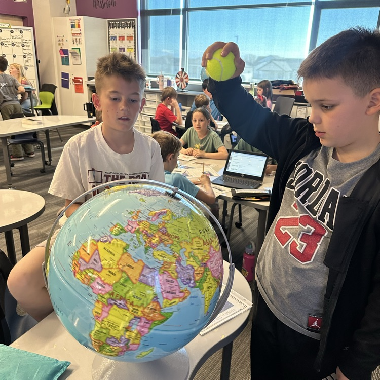 2 boys, one holding a tennis ball over a globe