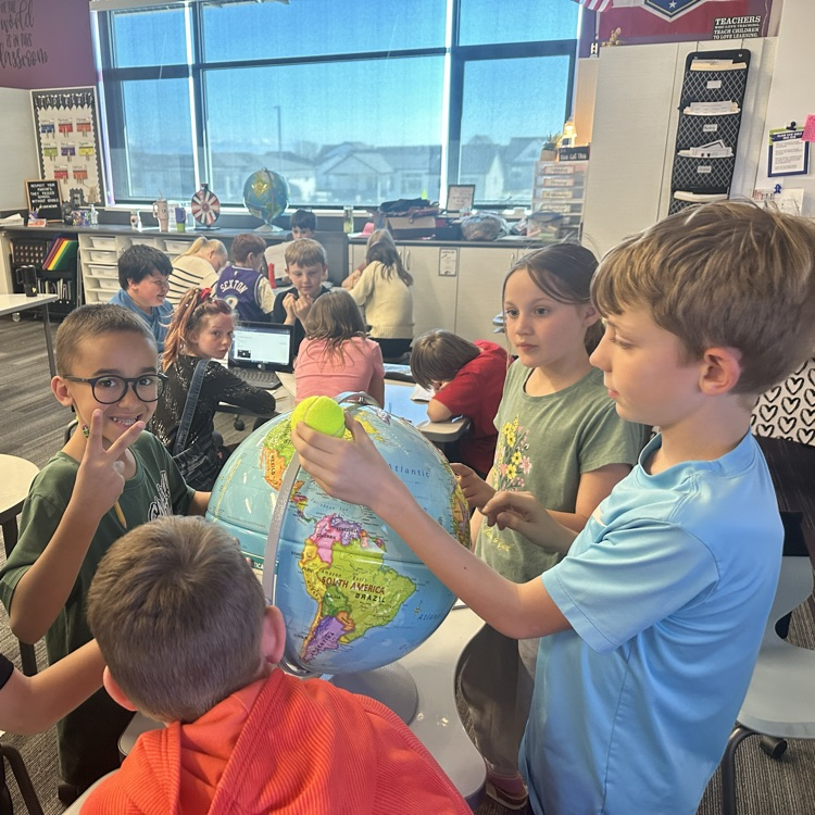 group of students holding a tennis ball above the globe