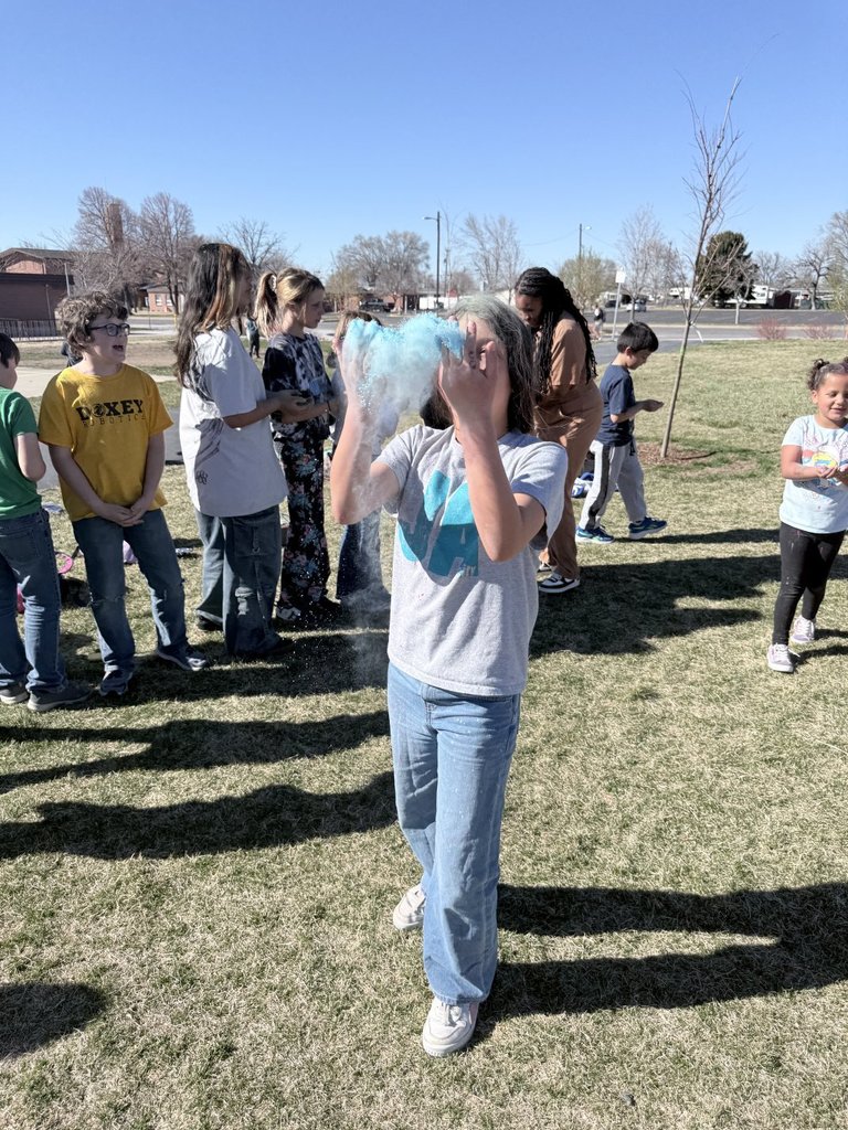 A student tosses a vibrant cloud of light blue powder into the air, momentarily hiding her face in a burst of color.