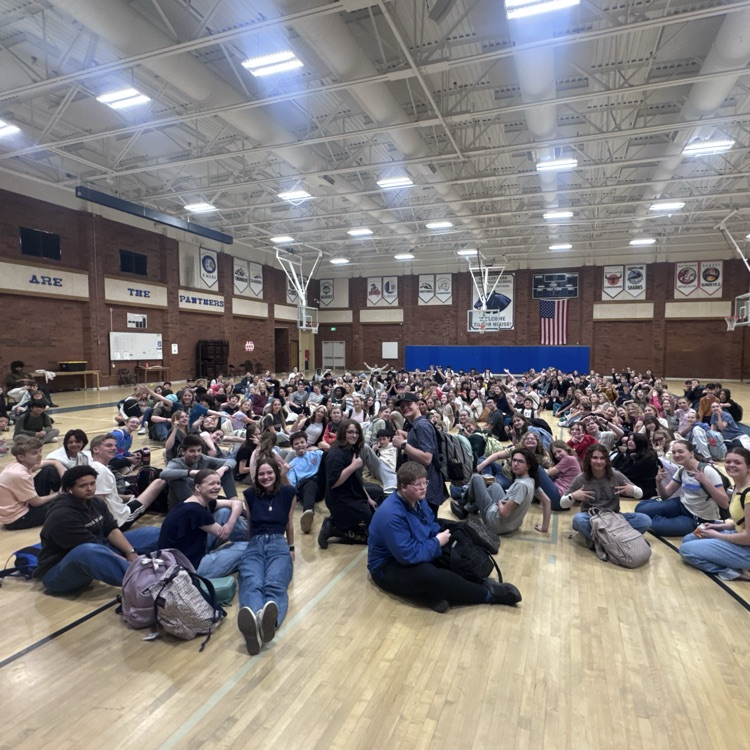 over 200 students sit on the gym floor and smile for the camera 