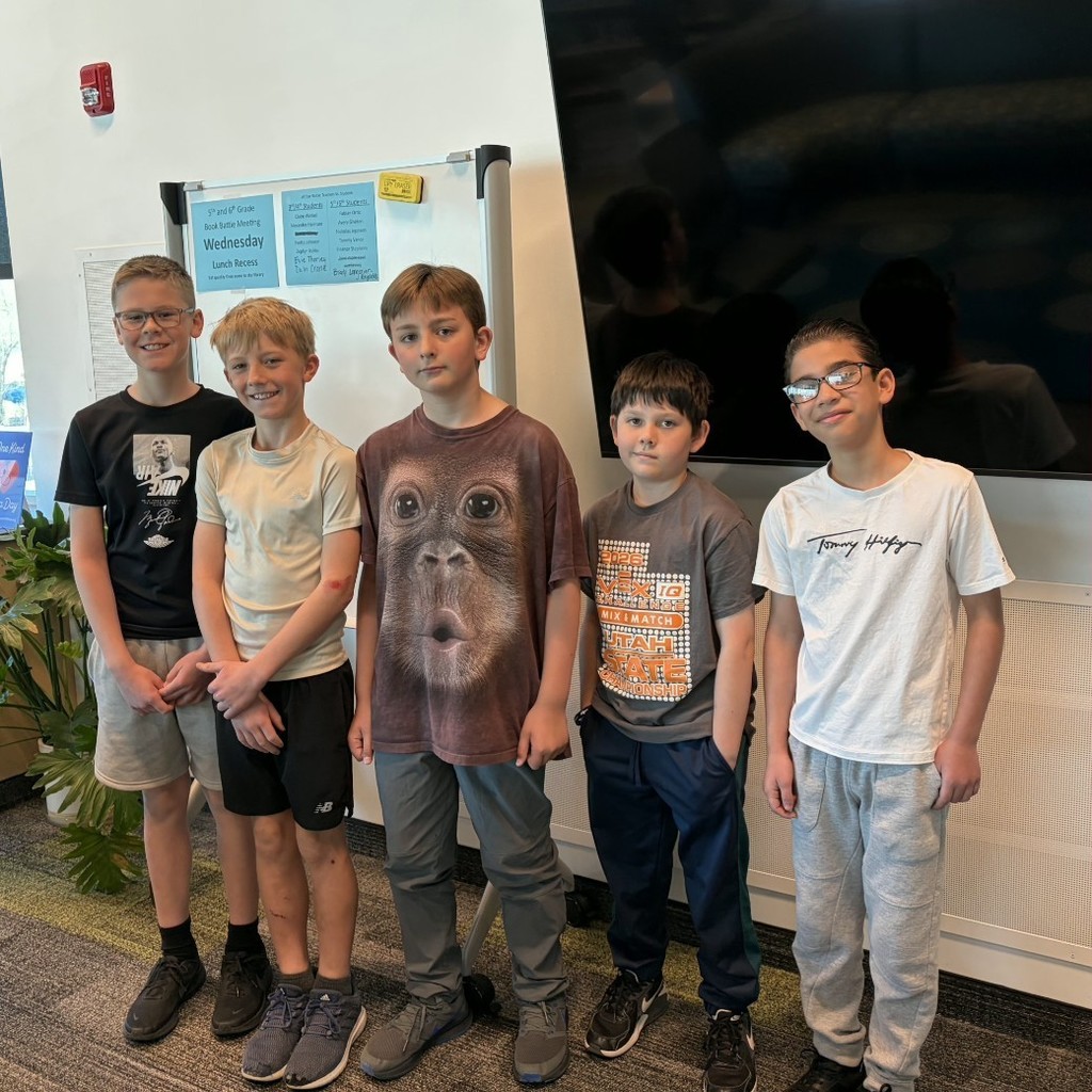 Five upper elementary students stand together in front of a display screen during a Book Battle team meeting.