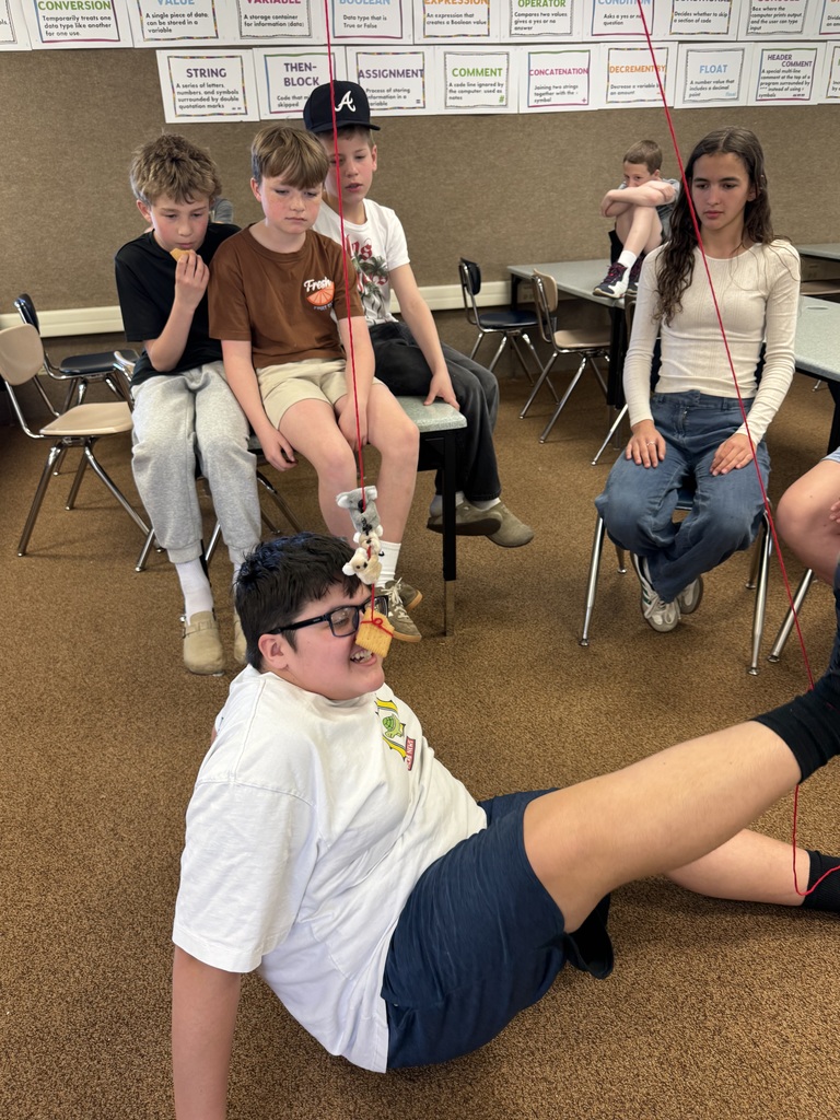 A photo of kids doing a STEM activity with string tied around their ankles