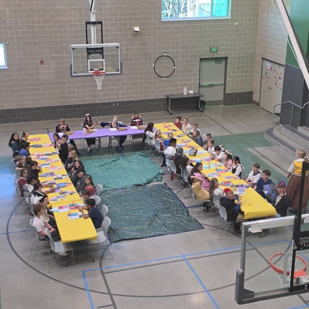 Students in crowns, cloaks, and medieval attire gather around a feast table at Bountiful Elementary’s 6th grade Medieval Feast.