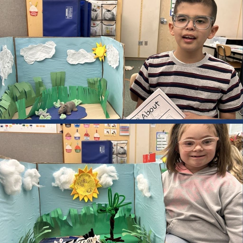 Students sitting next to their animal habitats created using clay, paper, and art supplies.