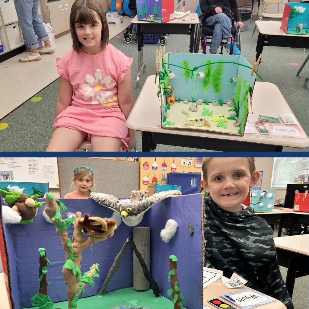 Students sitting next to their animal habitats created using clay, paper, and art supplies.