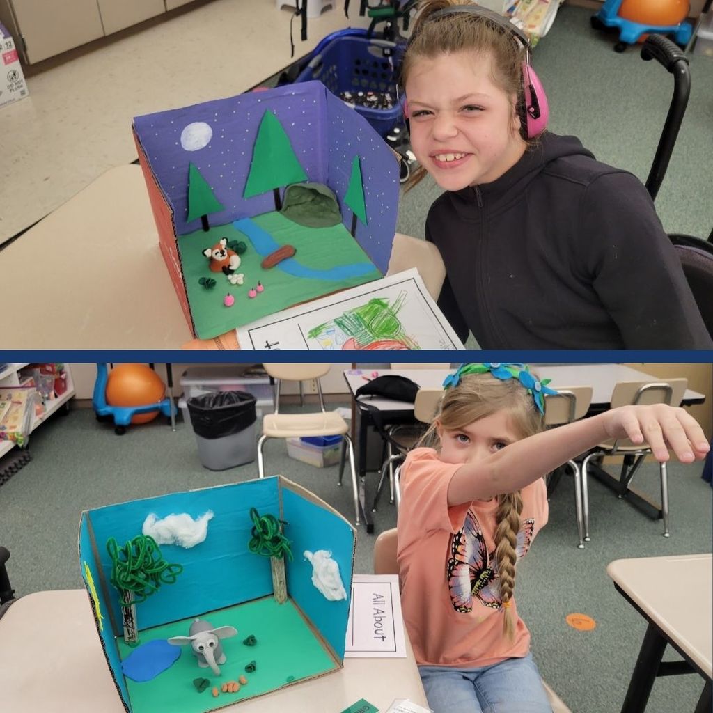 Students sitting next to their animal habitats created using clay, paper, and art supplies.