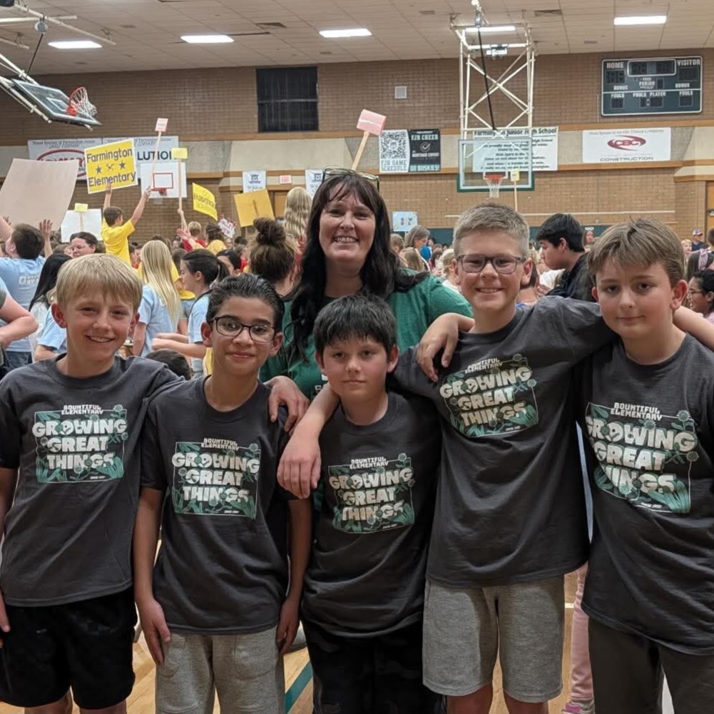 Mrs. Berge stands with five Bountiful Elementary students in matching school shirts at a crowded book event in a school gym.