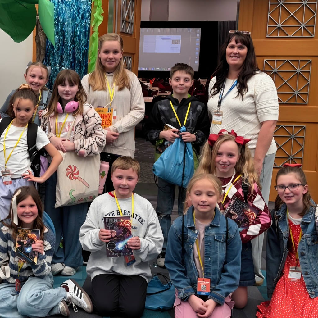 Mrs. Berge poses with a group of Bountiful Elementary students at Story Con, where students wear name badges and hold books and bags.