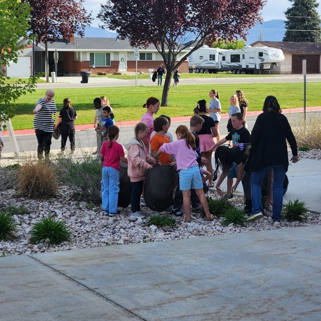 Students work together outside the school to pick up trash and pull weeds.