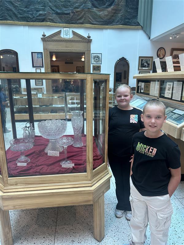 two grils standing next to a glass case with glass bowls inside