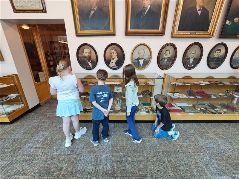 kids looking in glass cases and portraits above on the wall