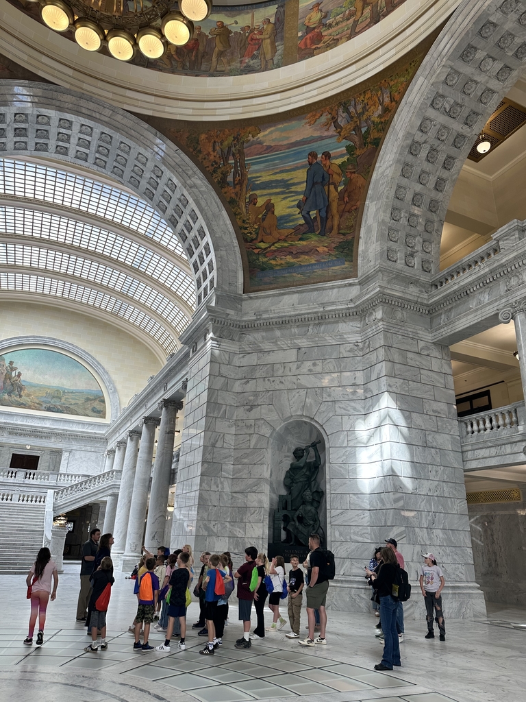 group of people standing in a large open area with colorful artwork above of a men and native americans