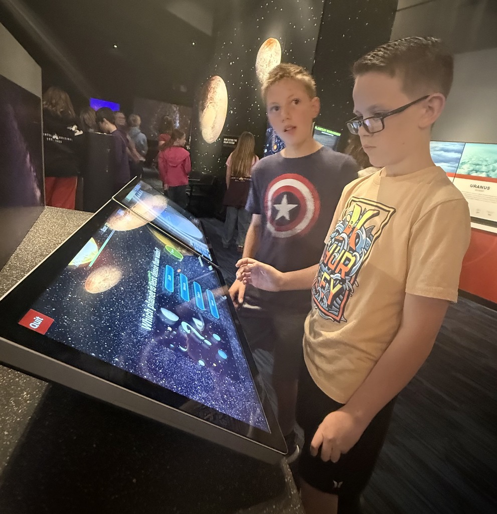 two boys in front of a large computer screen