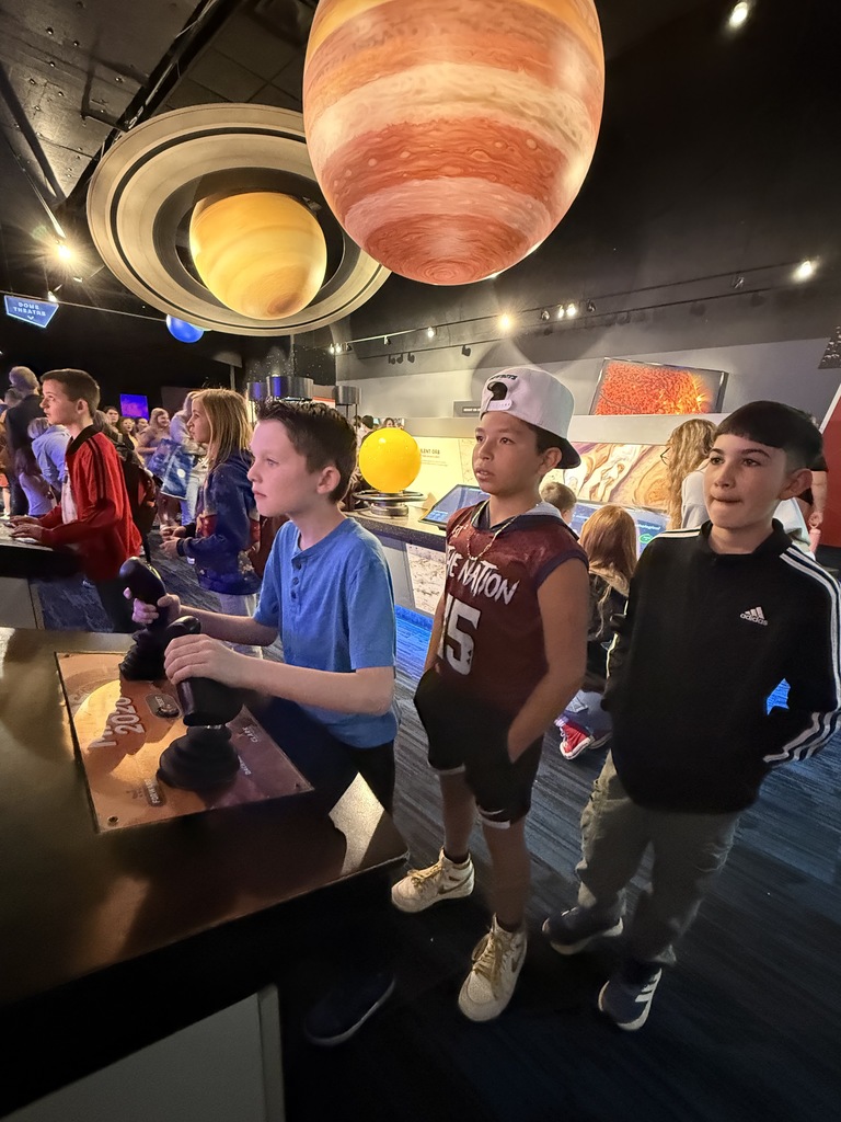 boys using joy sticks to play something and a large planet is above them