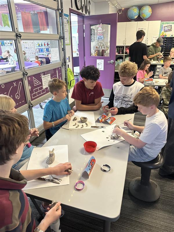 groups of boys sitting around a table while they use tools to decorate clay projects