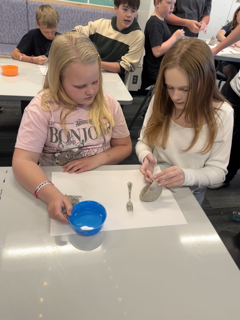 two girls, one holding a blue bowl with water and the other sculpting clay