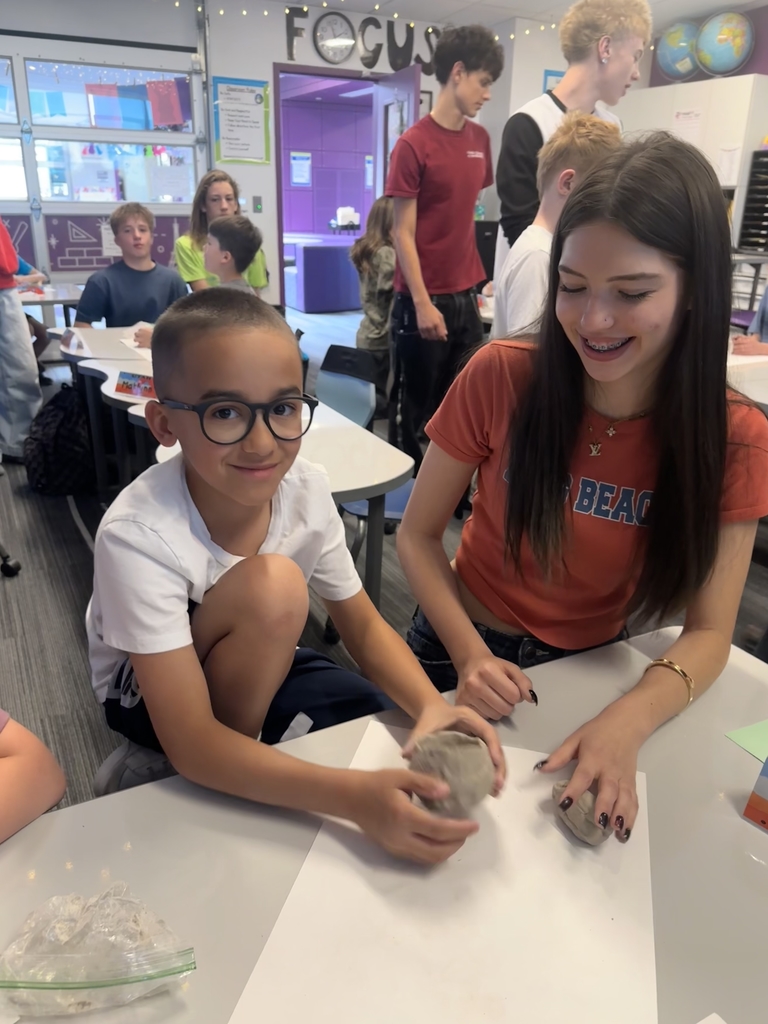 boy with glasses and girl smiling while holding clay on a desk