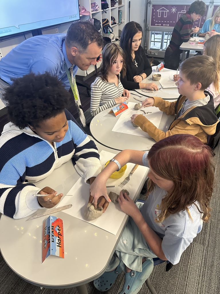 man bending down talking with a group of students as they make things out of clay