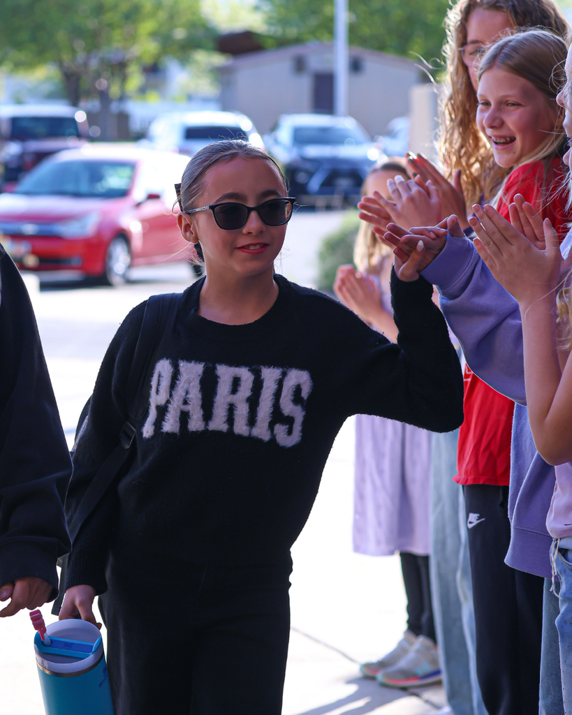 A student in a sweater that reads "Paris" walks through a sea of people clapping for her.