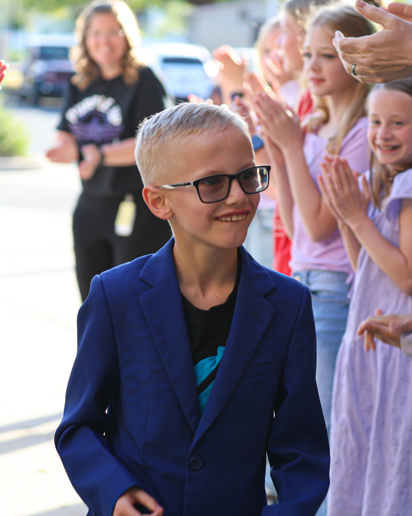 A student wearing a blue blazer smiles as he walks through a crowd of people clapping for him. 