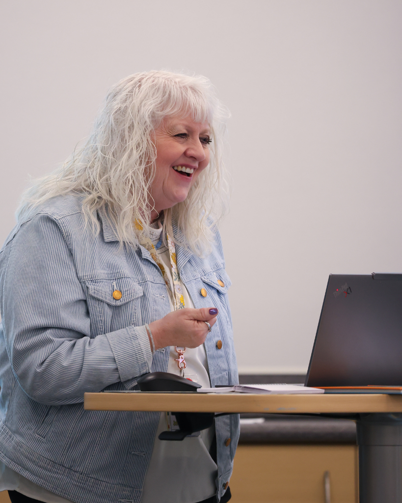 Someone at a desk with a laptop smiling at someone out of frame.