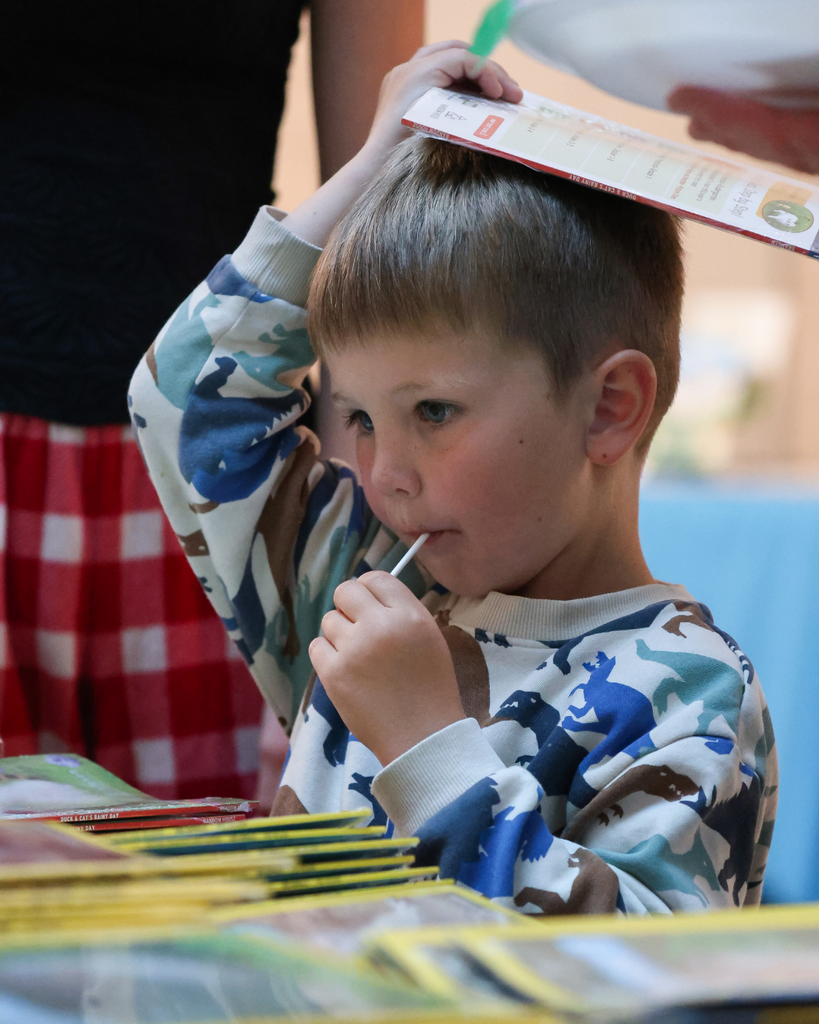 A student eating a sucker holds a book over his head.