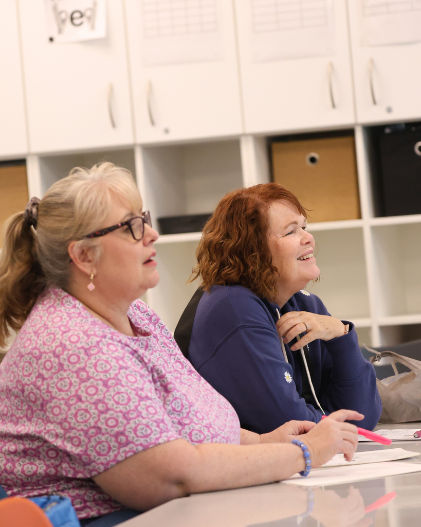 Two adults sitting in a classroom smiling.