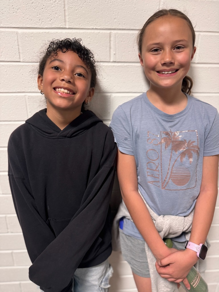 Two 4th graders standing and smiling in their school hallway.