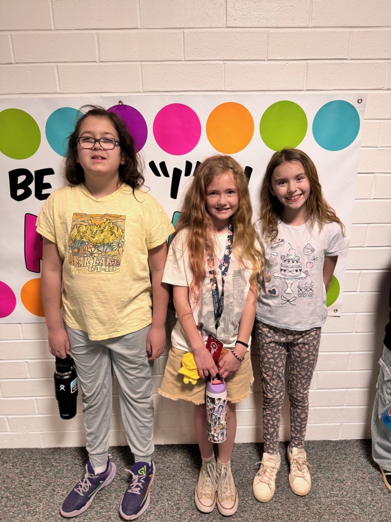 Three fourth graders standing and smiling together in school hallway.