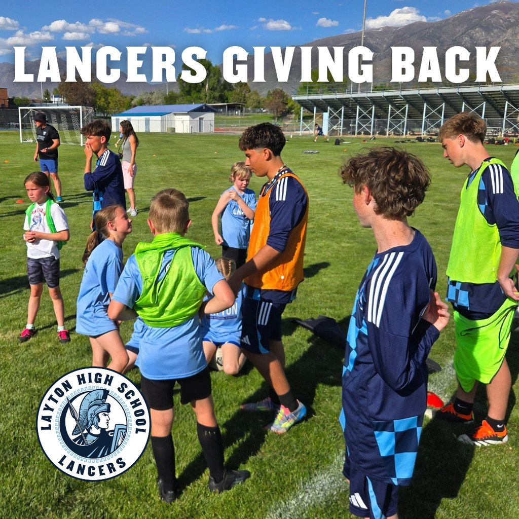 picture showing Lancer soccer players working with young children on their skills.  caption says "Lancers giving back"