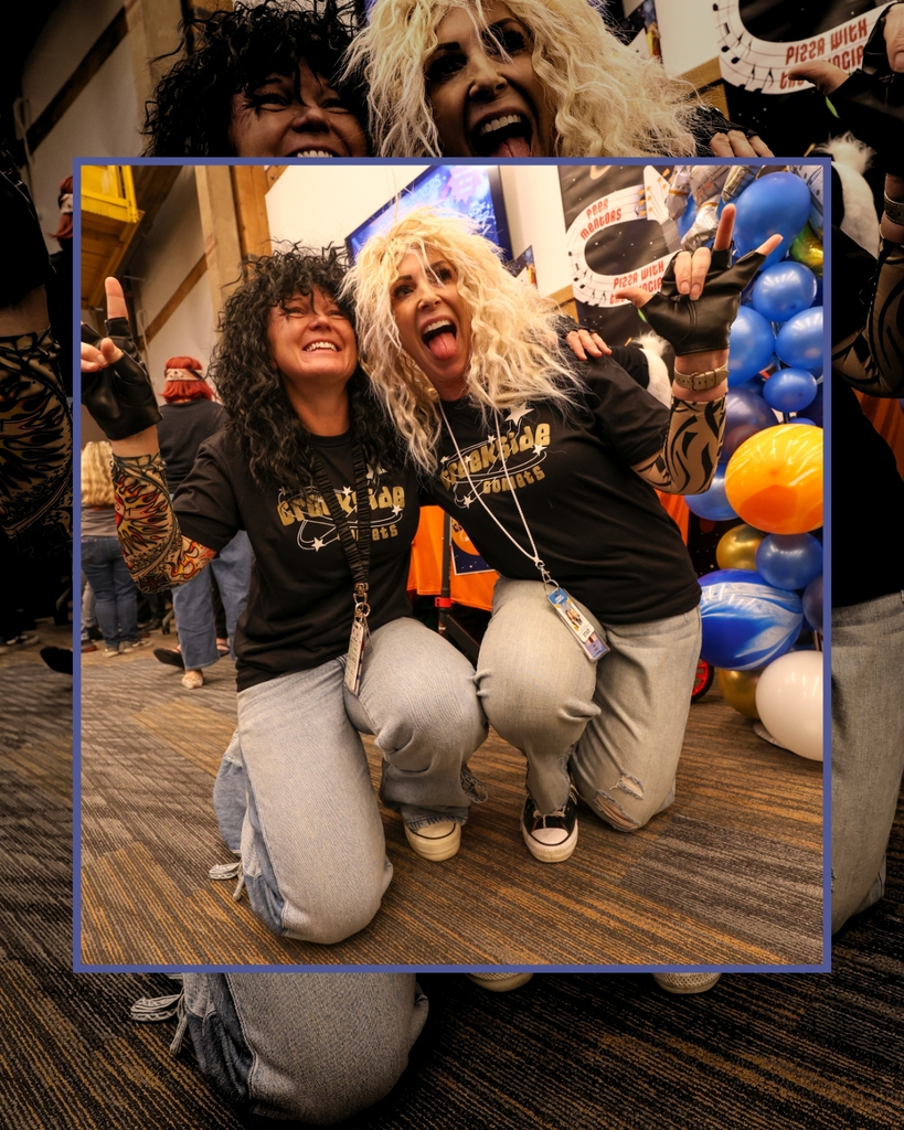 Two people wearing kiss-style blonde and brown wigs give us the "rock" sign. 