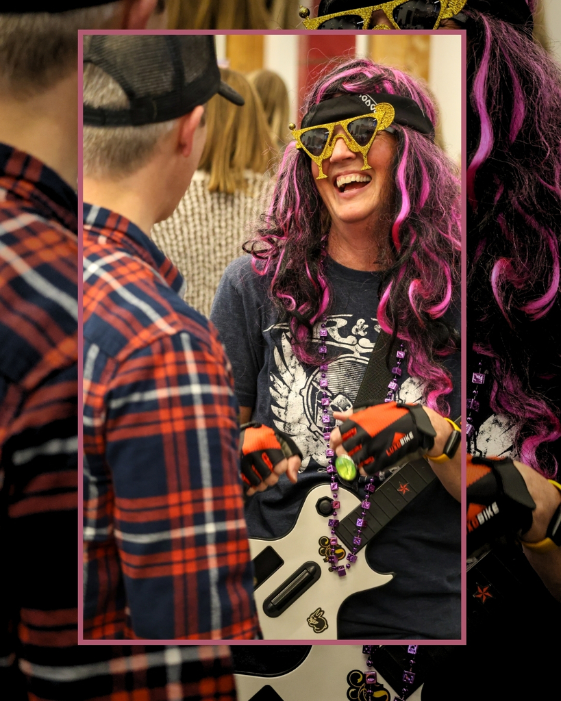 Someone dressed up in a pink and black wig with gold margarita glasses and wearing a guitar laughs. 