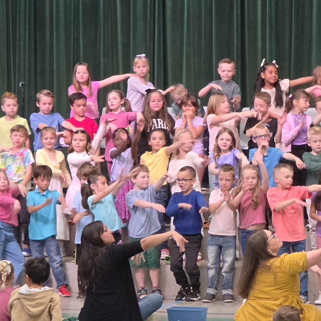 First-grade students perform hand motions on stage while teachers lead them from the front during the Spring Sing.
