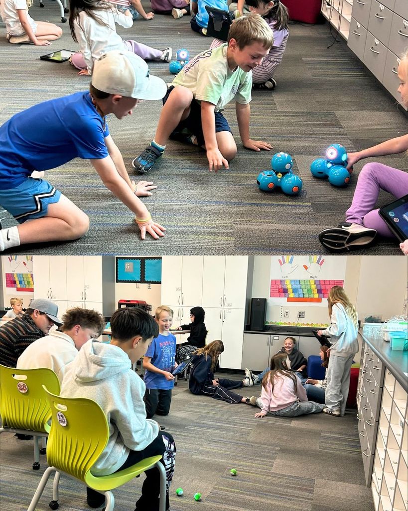 Students sit on the classroom floor interacting with small blue robots, while nearby older students work together in groups, using tablets and collaborating on activities.