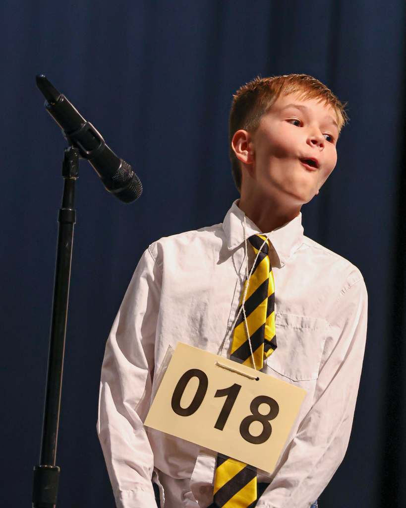 A student wearing a #18 card around his neck looks to the right in awe. 
