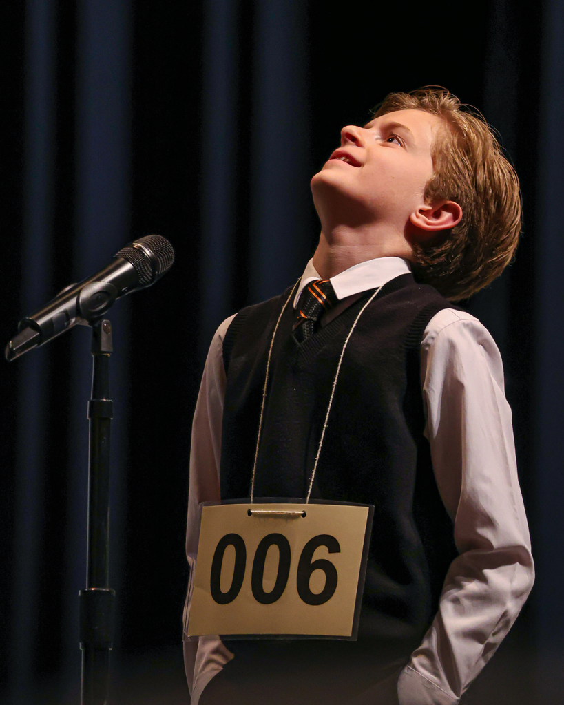 A student standing next to a microphone tilting his head back looking at the ceiling. 